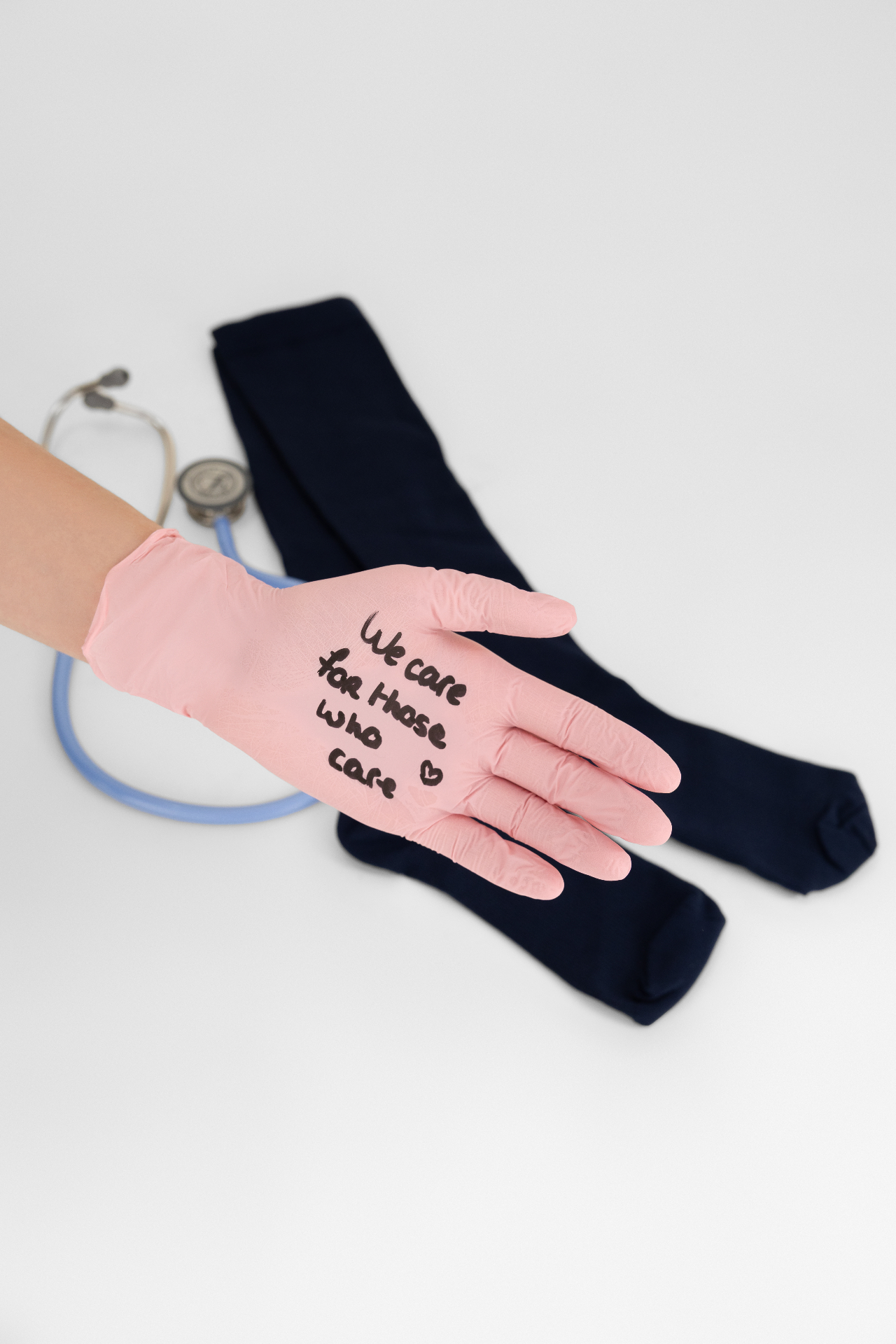 Roze handschoen met de boodschap we care for those who care op een marineblauwe Repose compressiesok en stethoscoop